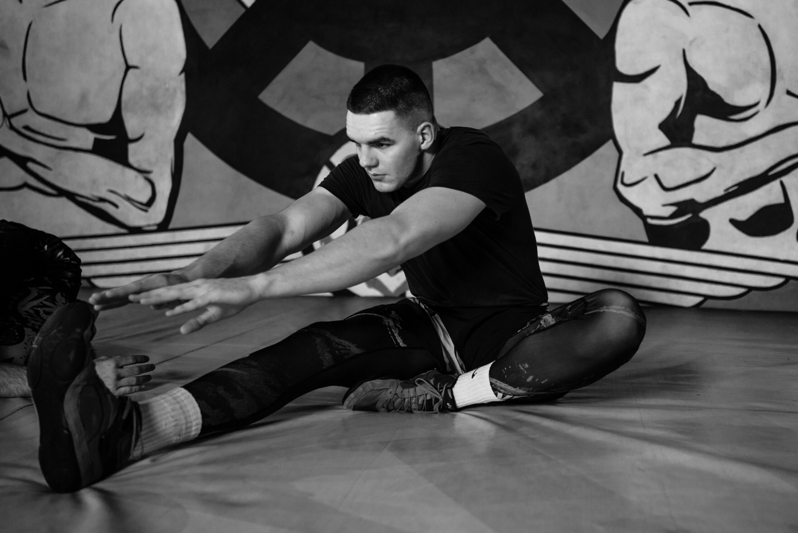 Focused adult male athlete stretching on a gym mat amidst training, capturing strength and concentration.
